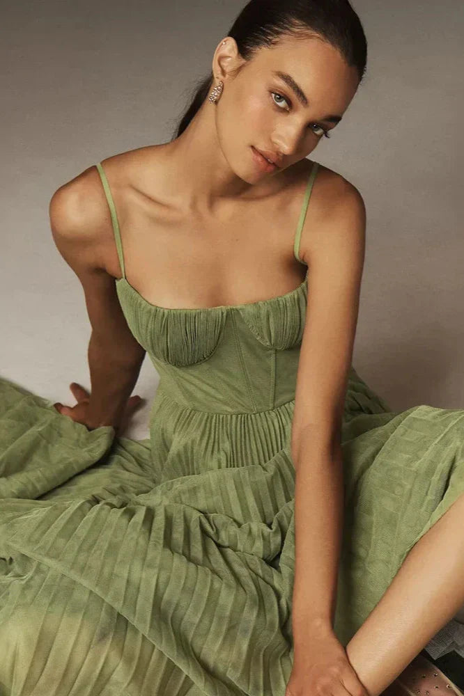Model sitzt in einem stilvollen Isabella Plissiertes Tüll-Midikleid von Fadenburg, zeigt die fließende Textur und den eleganten Abschluss des Kleides.